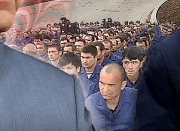 A long column of detained men in uniform, heads shaved, under guard.